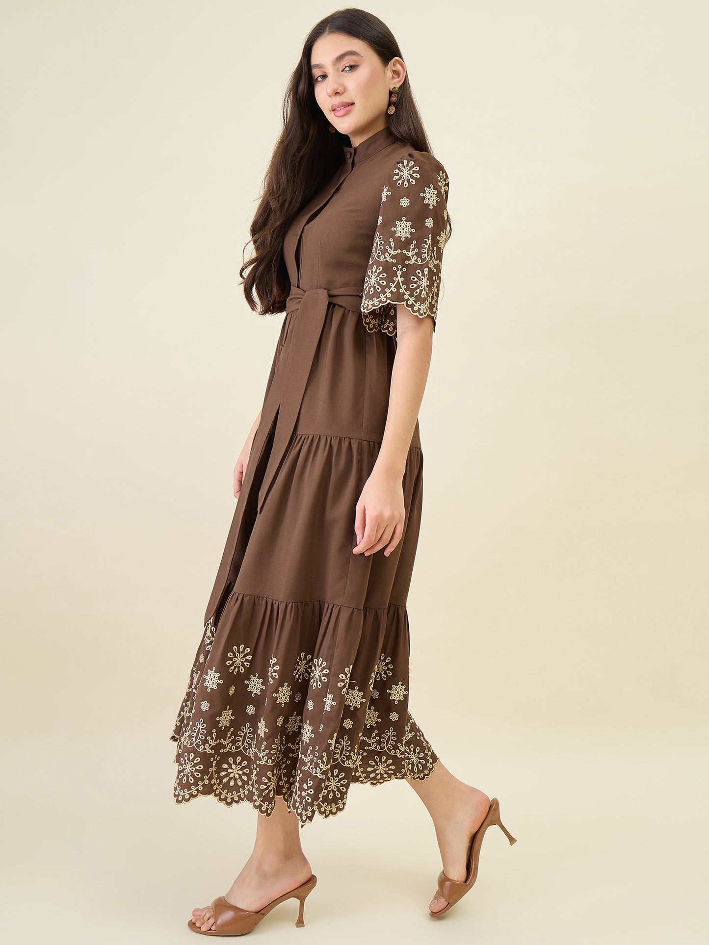 Woman wearing a brown dress with floral embroidery on a beige background