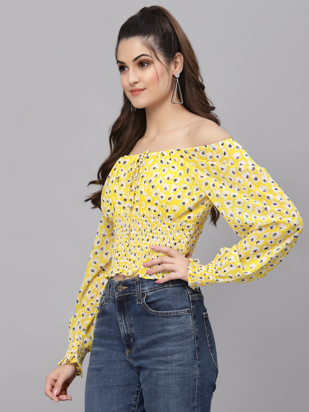 Woman wearing a yellow floral off-shoulder top and blue jeans on a gray background