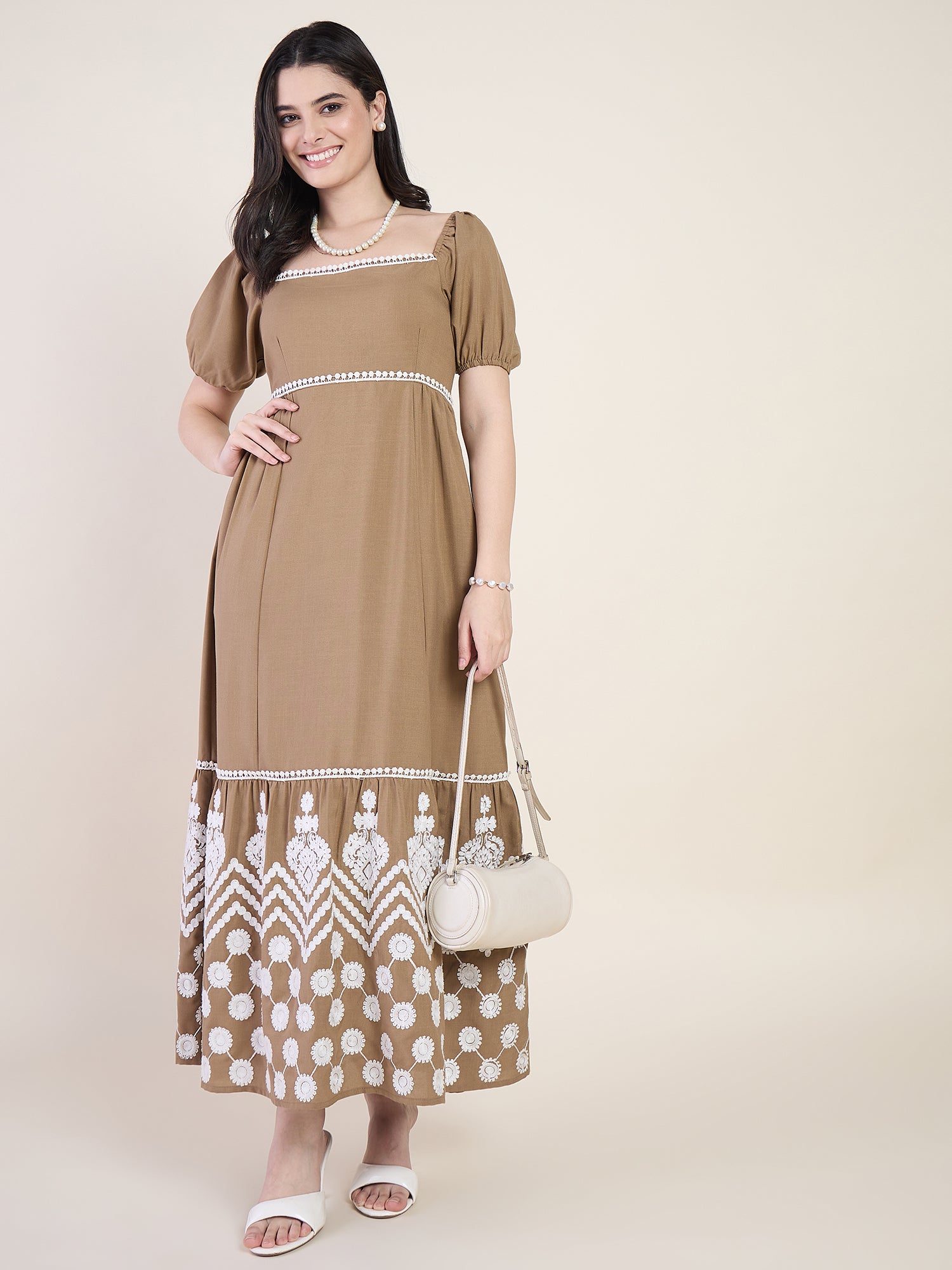 Woman wearing a brown dress with white patterns, holding a matching handbag against a plain background