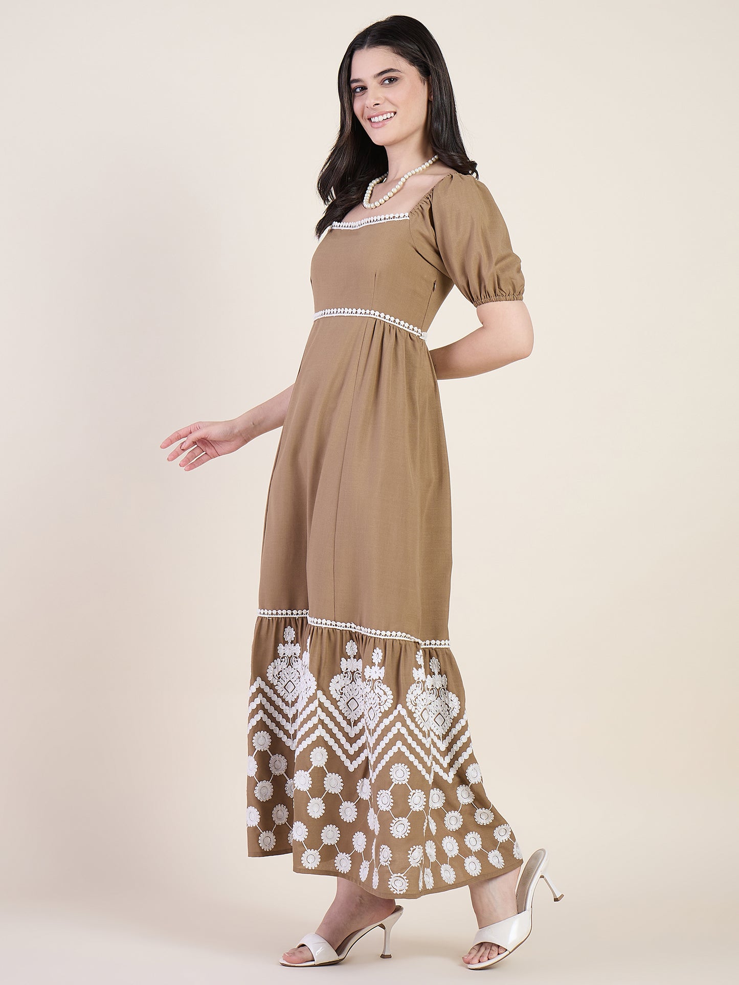 Woman wearing a brown dress with white embroidery on a beige background