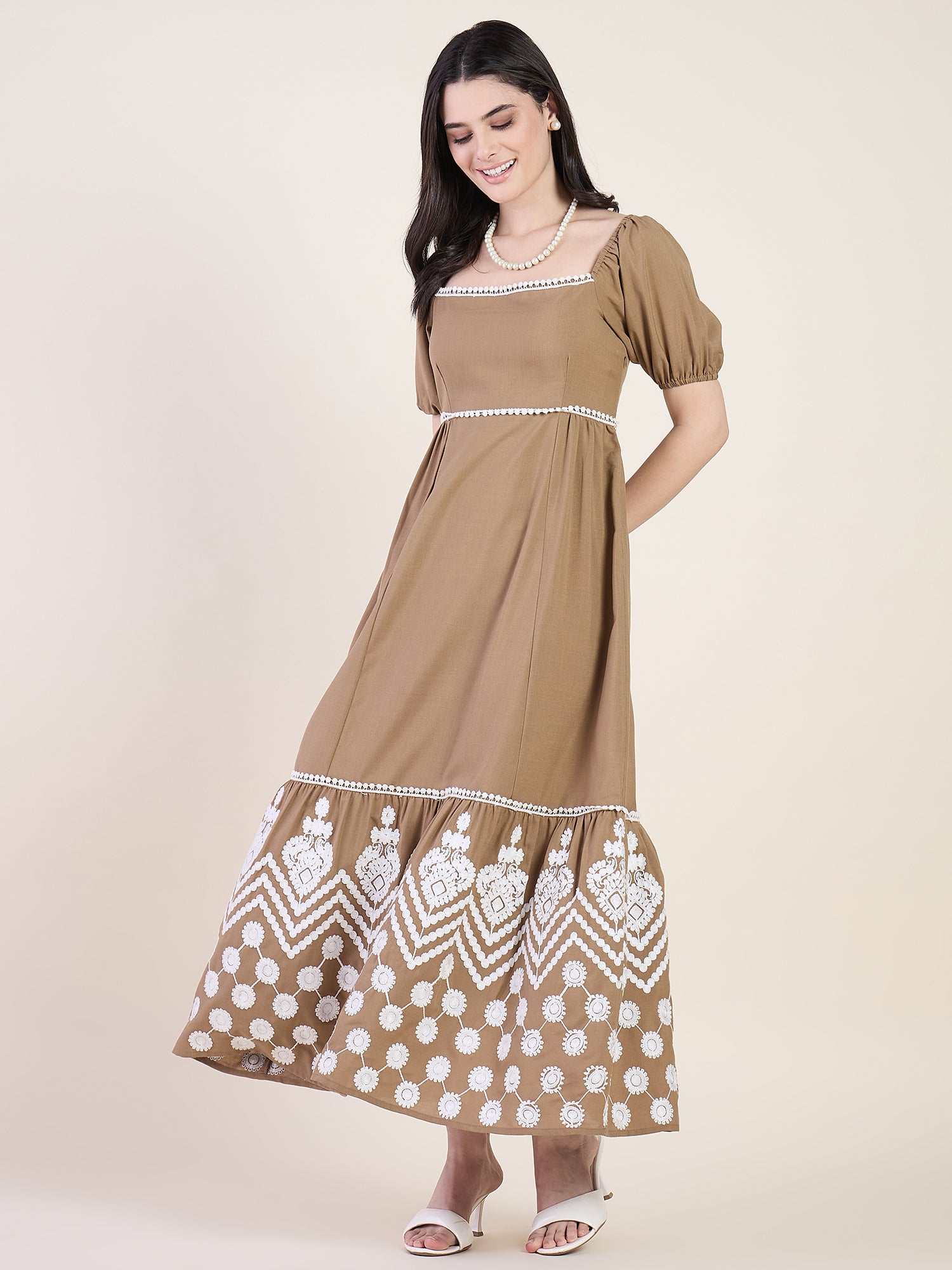 Woman wearing a brown dress with white embroidery on a beige background