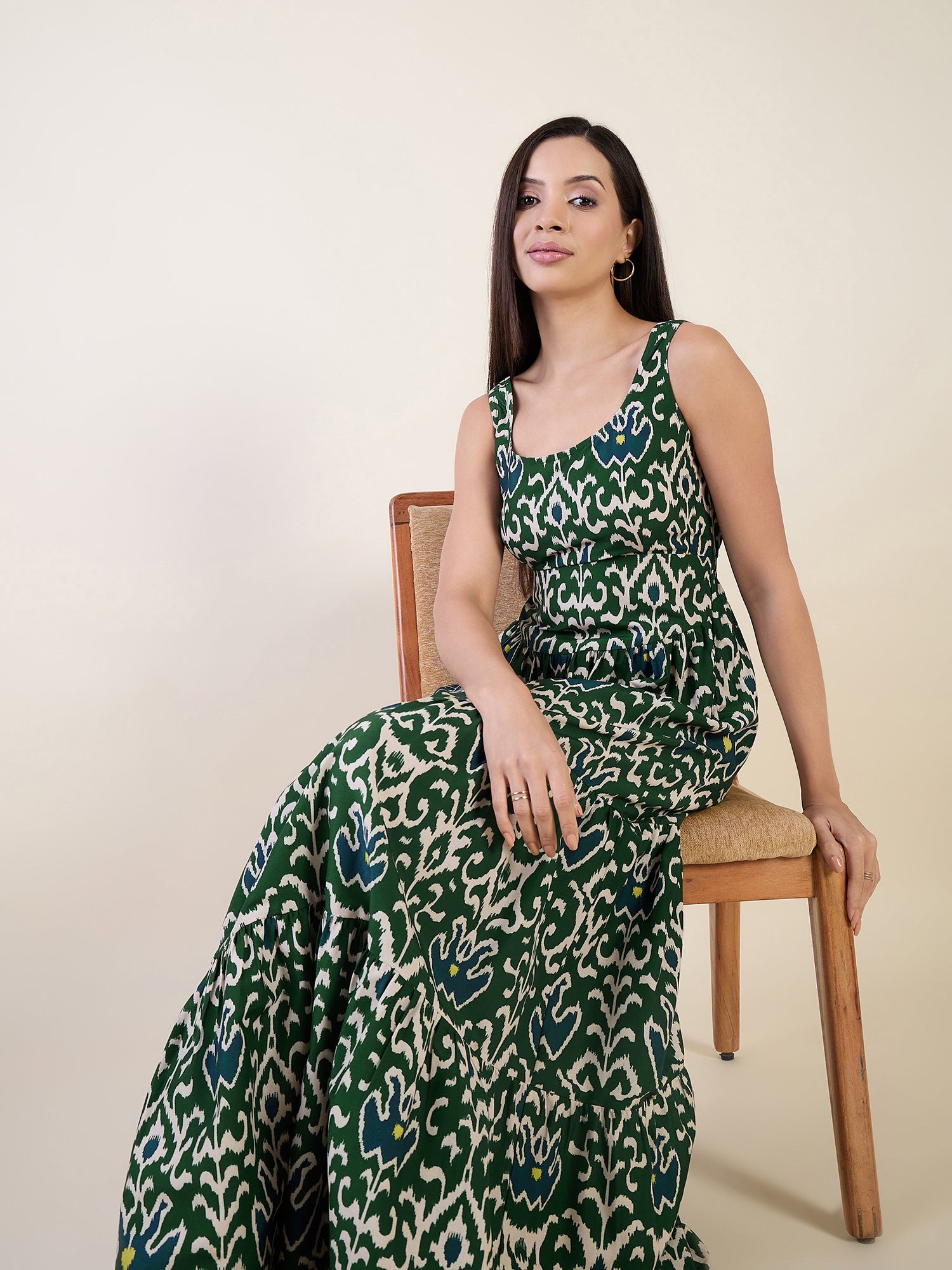 Woman wearing a green and white patterned dress sitting on a chair against a beige background