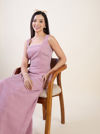 Woman wearing a pink checkered dress sitting on a wooden chair against a plain background