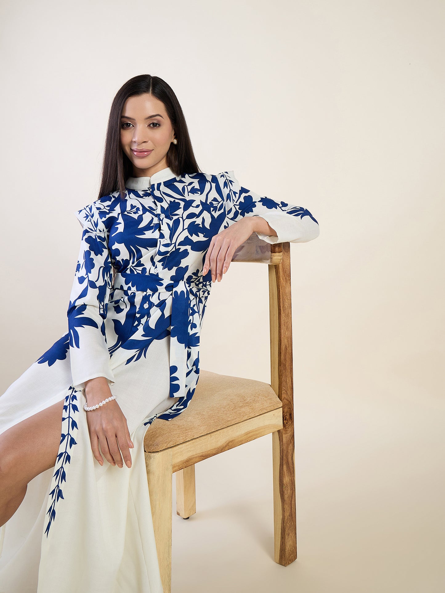 Woman wearing a blue and white floral dress sitting on a wooden chair against a beige background