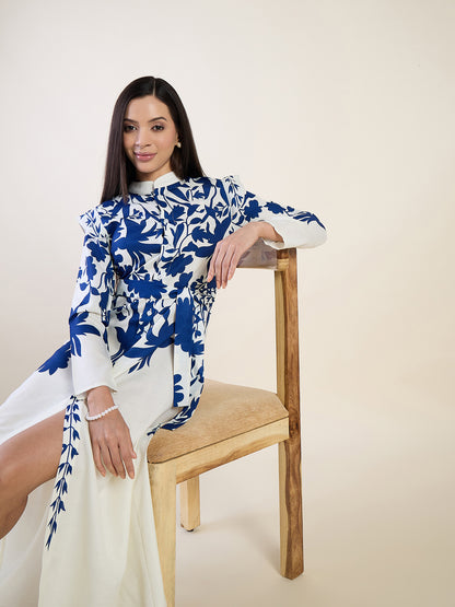 Woman wearing a blue and white floral dress sitting on a wooden chair against a beige background