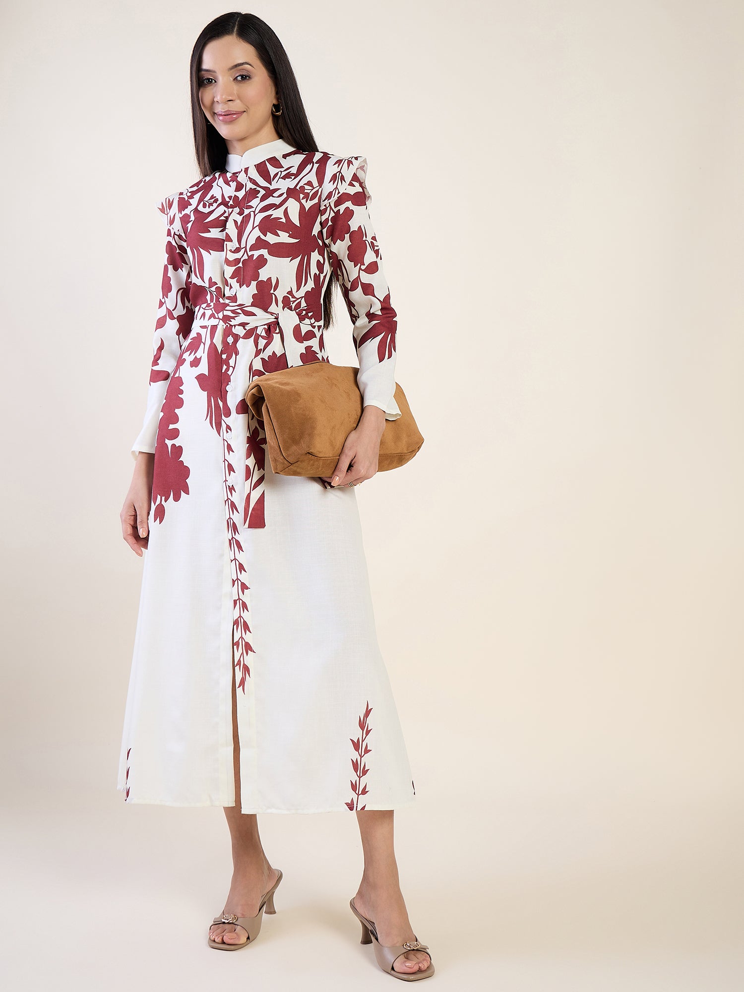 Woman wearing a white dress with red floral patterns, holding a brown clutch against a white background