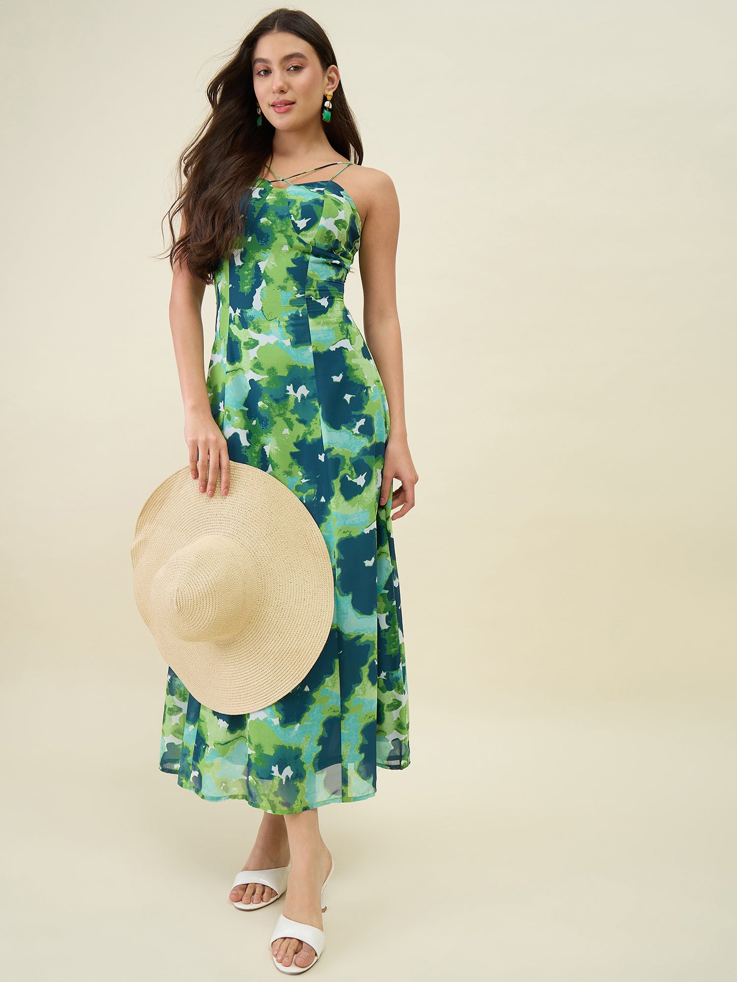Woman wearing a green floral dress holding a straw hat on a beige background