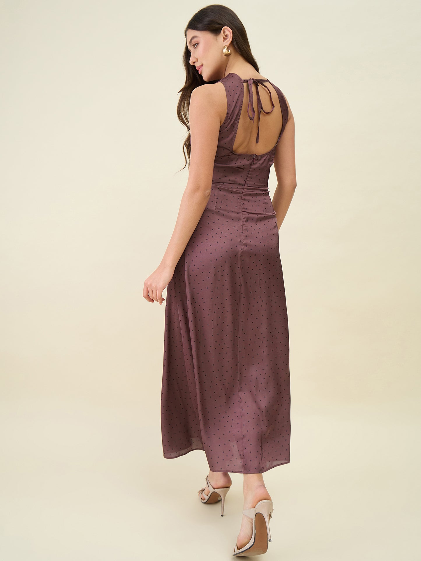 Woman wearing a brown dress with cut-out back on a beige background
