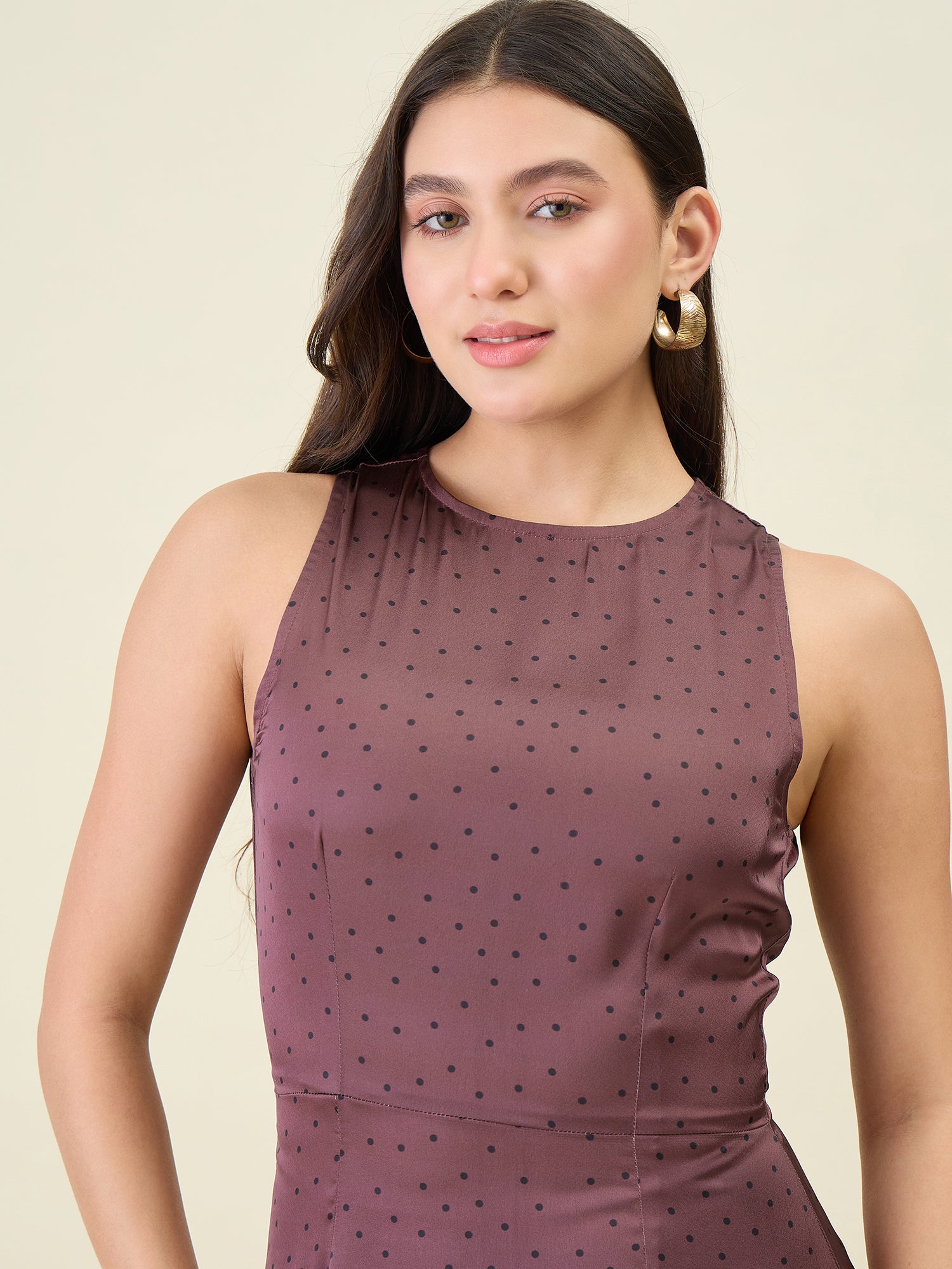 Woman wearing a sleeveless brown dress with black polka dots against a beige background