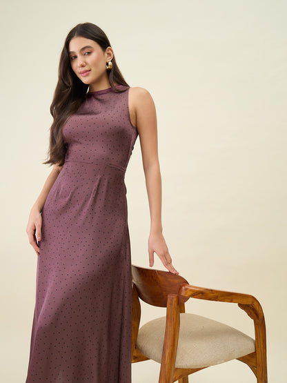 Woman wearing a long brown dress sitting on a wooden chair against a beige background