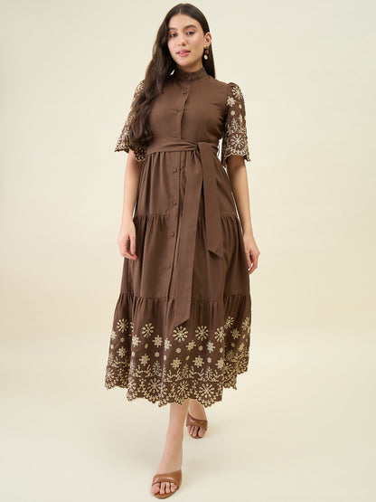 Woman wearing a brown dress with floral embroidery on a beige background