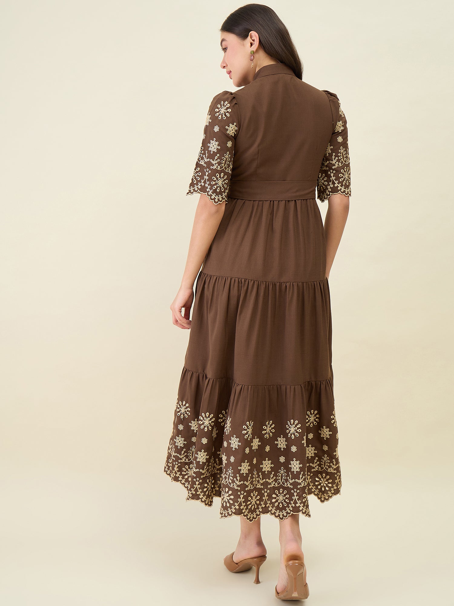 Woman wearing a brown dress with floral lace details on a beige background