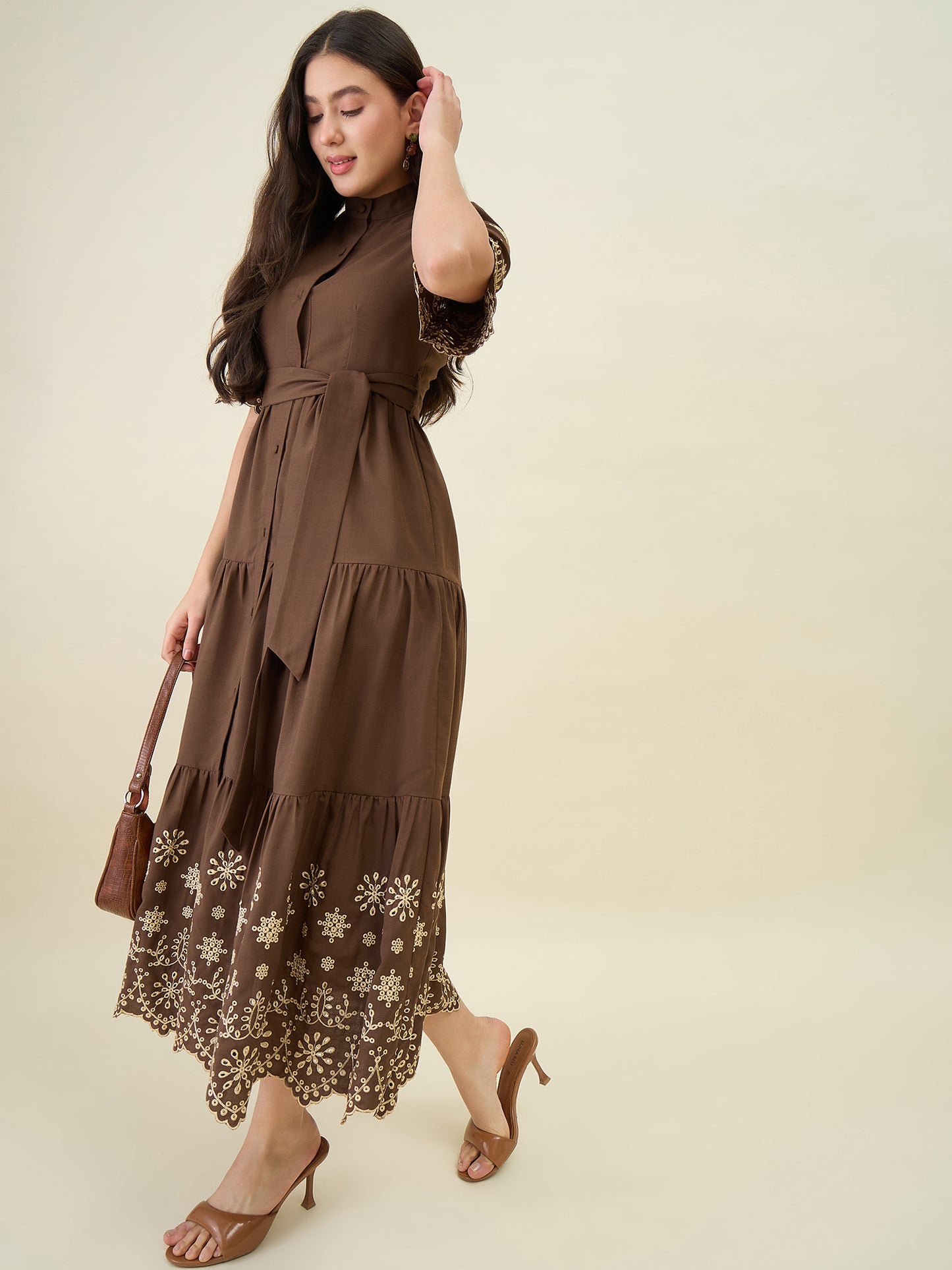 Woman wearing a brown dress with floral embroidery on a beige background