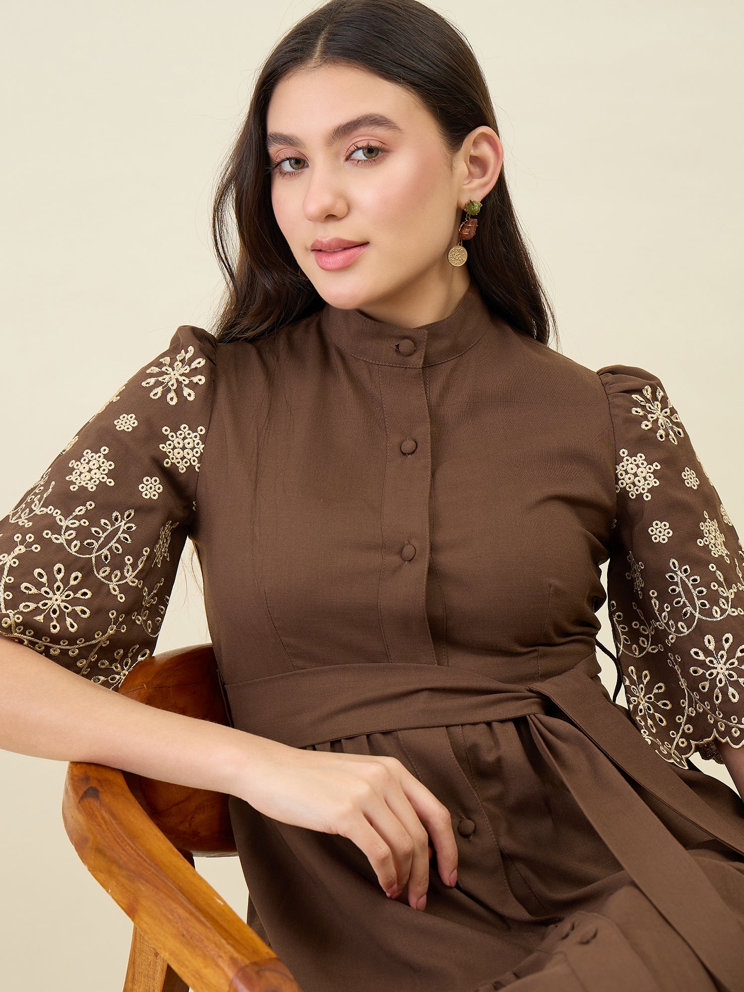Woman wearing a brown dress with floral patterns sitting on a wooden chair.