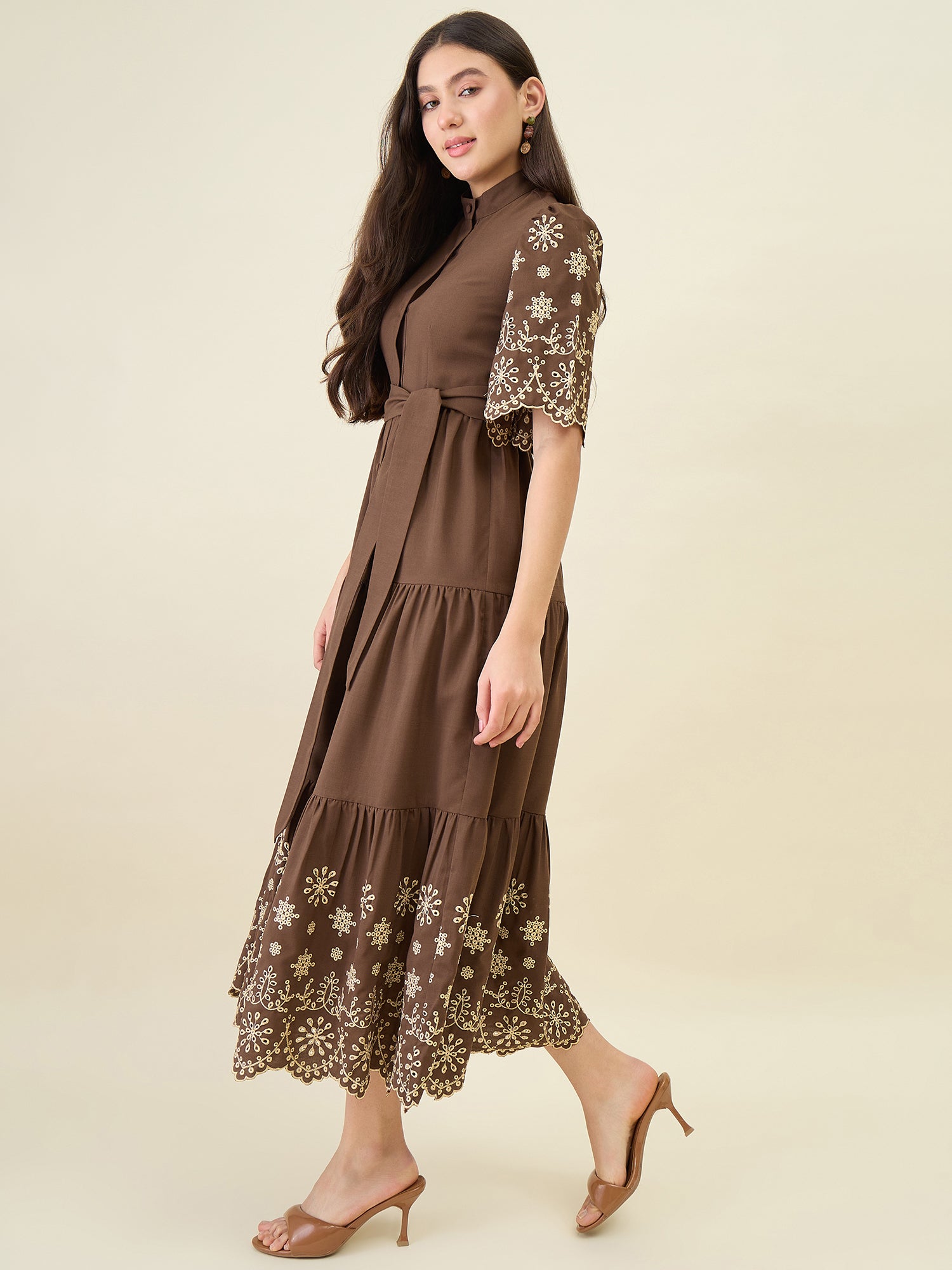 Woman wearing a brown dress with floral embroidery on a beige background
