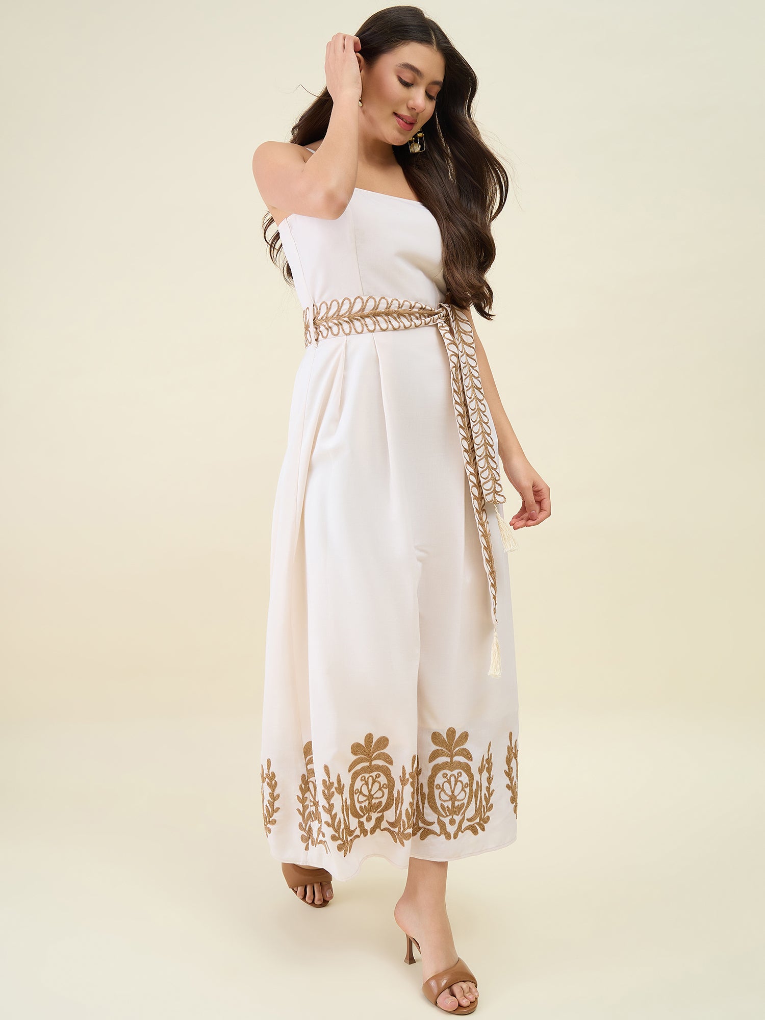 Woman wearing a white dress with gold embroidery on a beige background