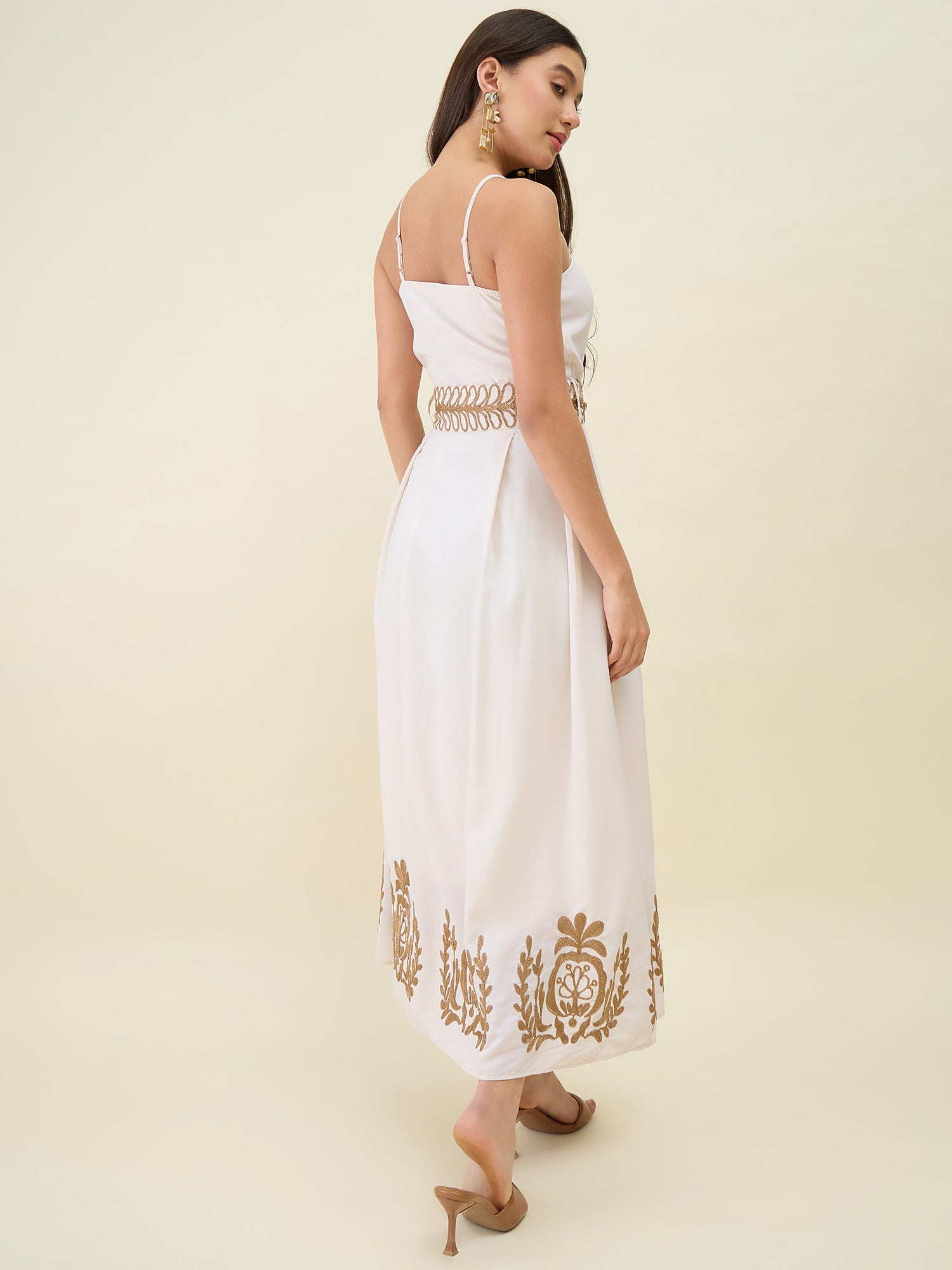 Woman wearing a white dress with gold embroidery on a beige background