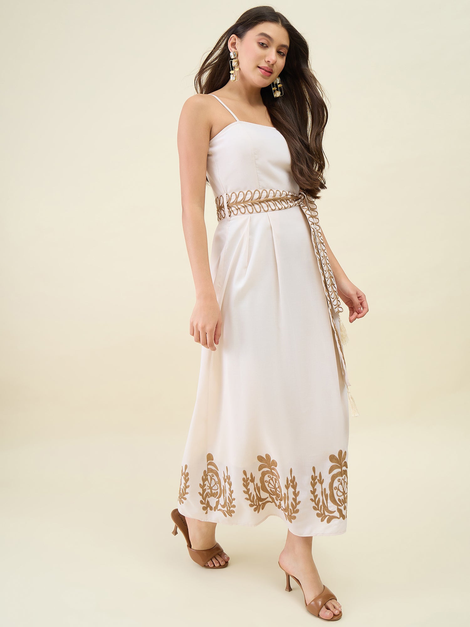 Woman wearing a white dress with gold embroidery on a beige background