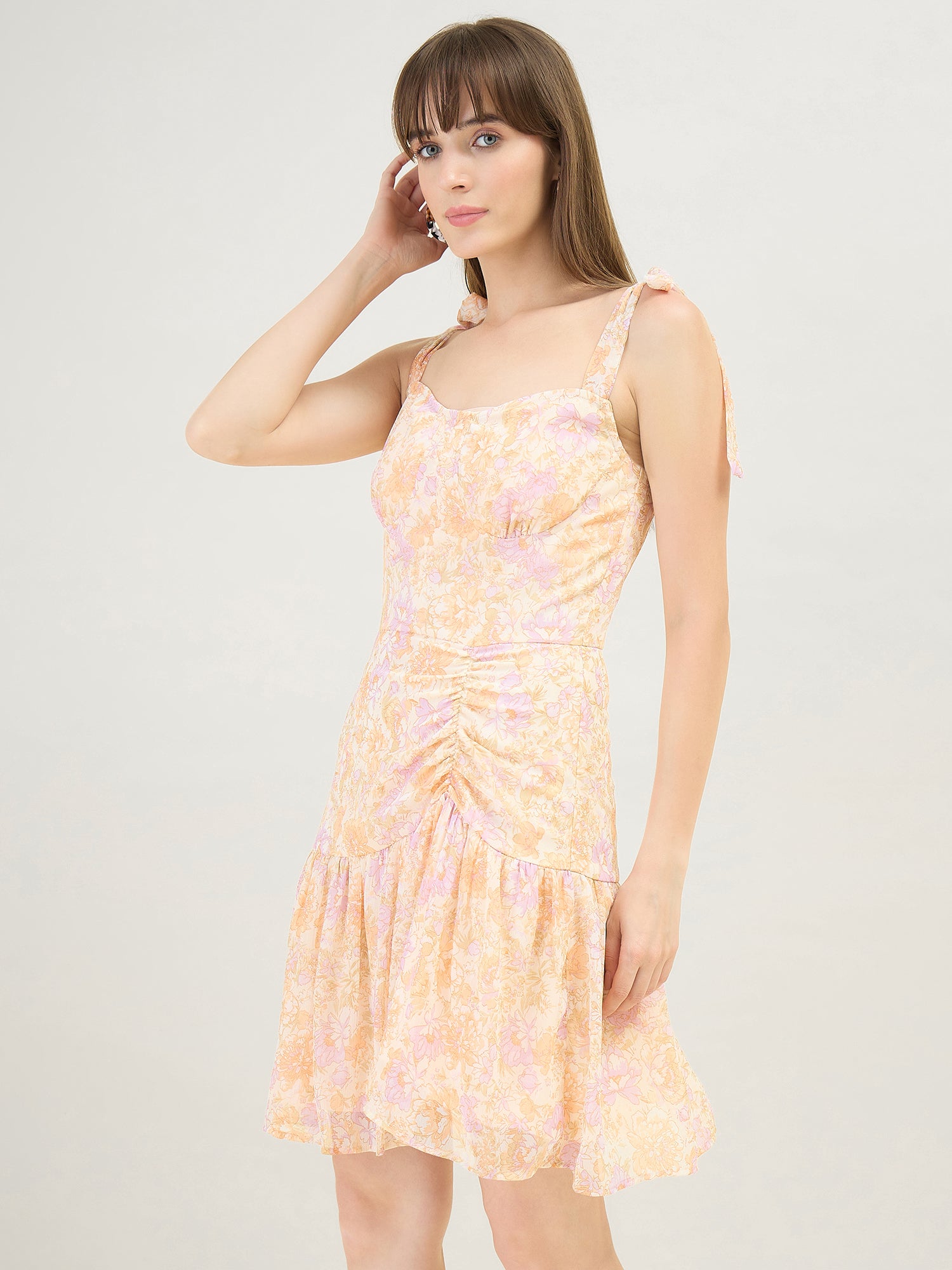 Woman wearing a peach color floral dress against a plain background