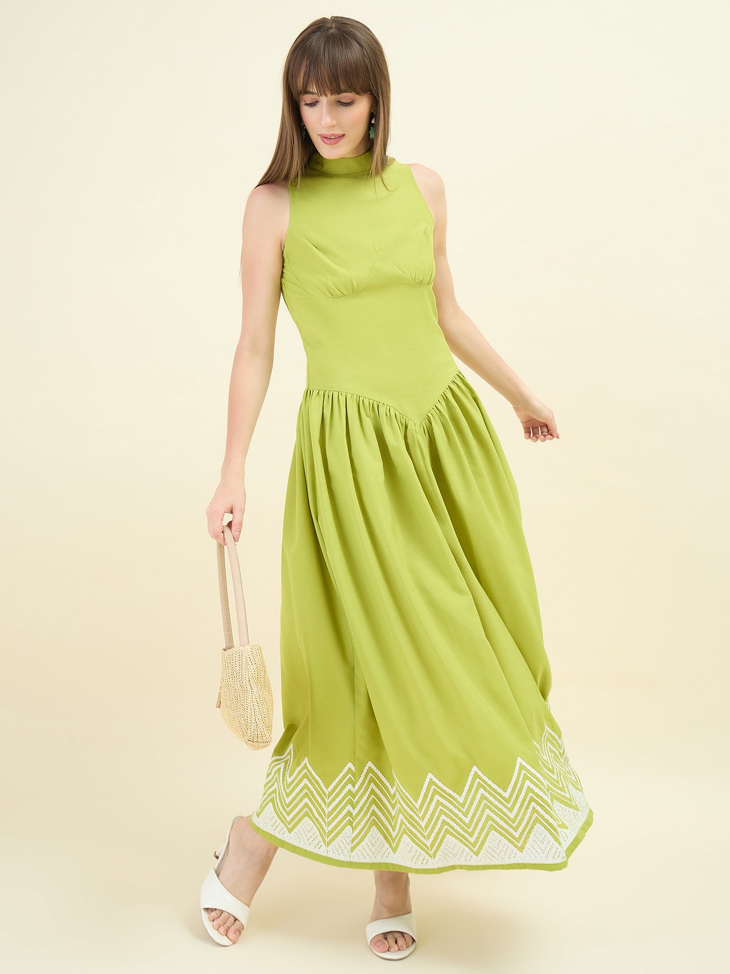 Woman wearing a sage green dress with white embroidery on a beige background