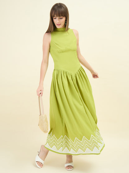 Woman wearing a sage green dress with white embroidery on a beige background