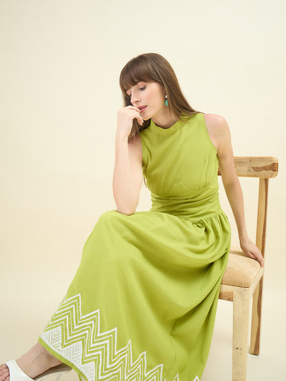 Woman wearing a green dress with white patterns, sitting on a wooden chair against a light background