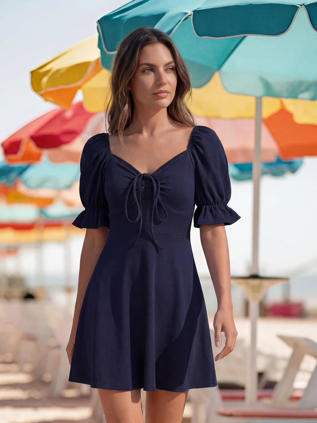 Woman in a navy blue dress standing in front of colorful beach umbrellas.