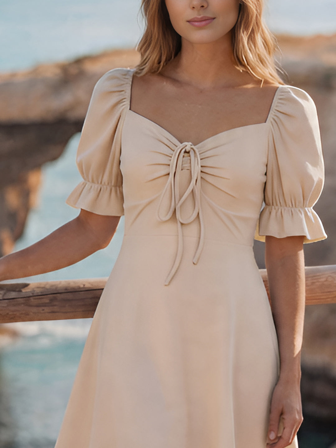 Woman wearing a cream dress with puff sleeves by a coastal background