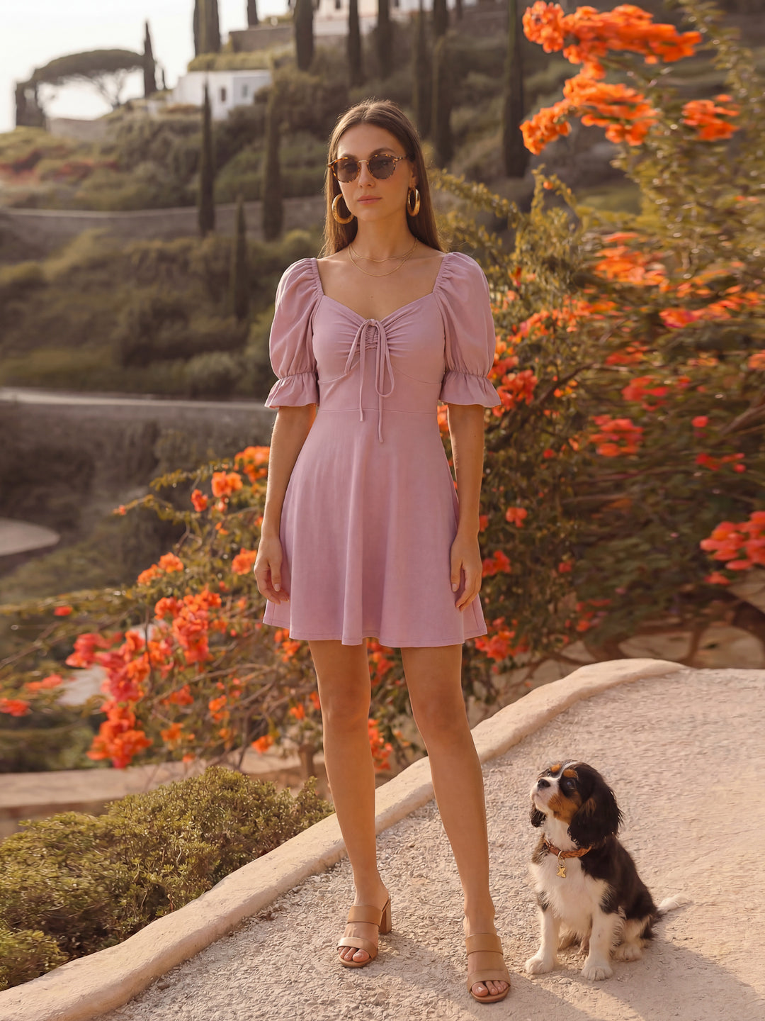 Woman in a mauve dress standing next to a dog with a scenic background