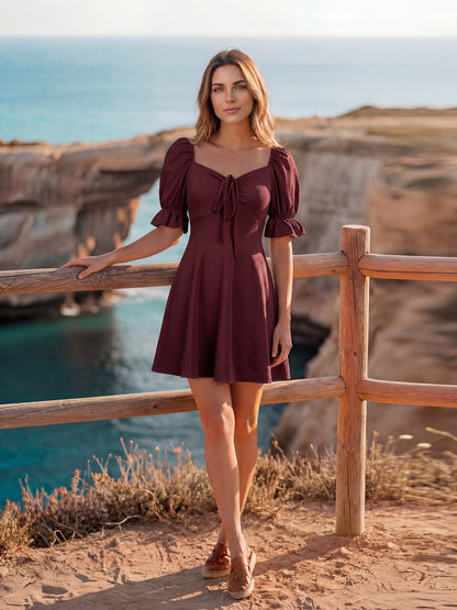 Woman in a Wine color dress standing by a wooden railing with ocean and cliffs in the background