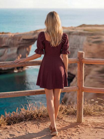 Woman in a burgundy dress standing on a cliff overlooking the ocean.