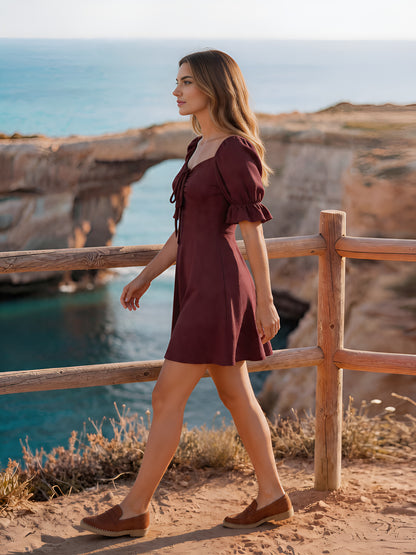 Woman in a wine color dress walking along a wooden railing with a scenic ocean view.