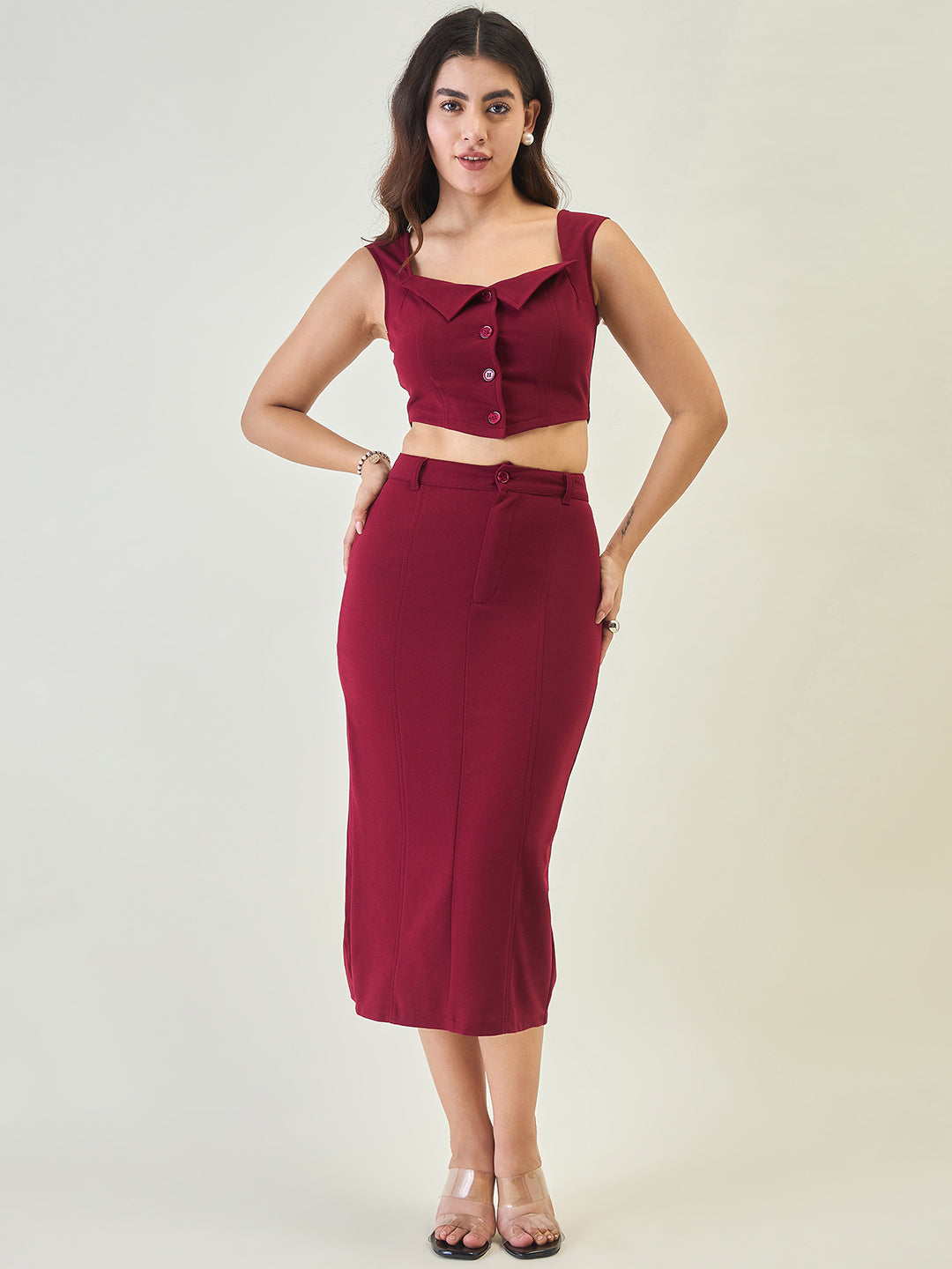 Woman wearing a maroon outfit with a top and skirt on a plain background