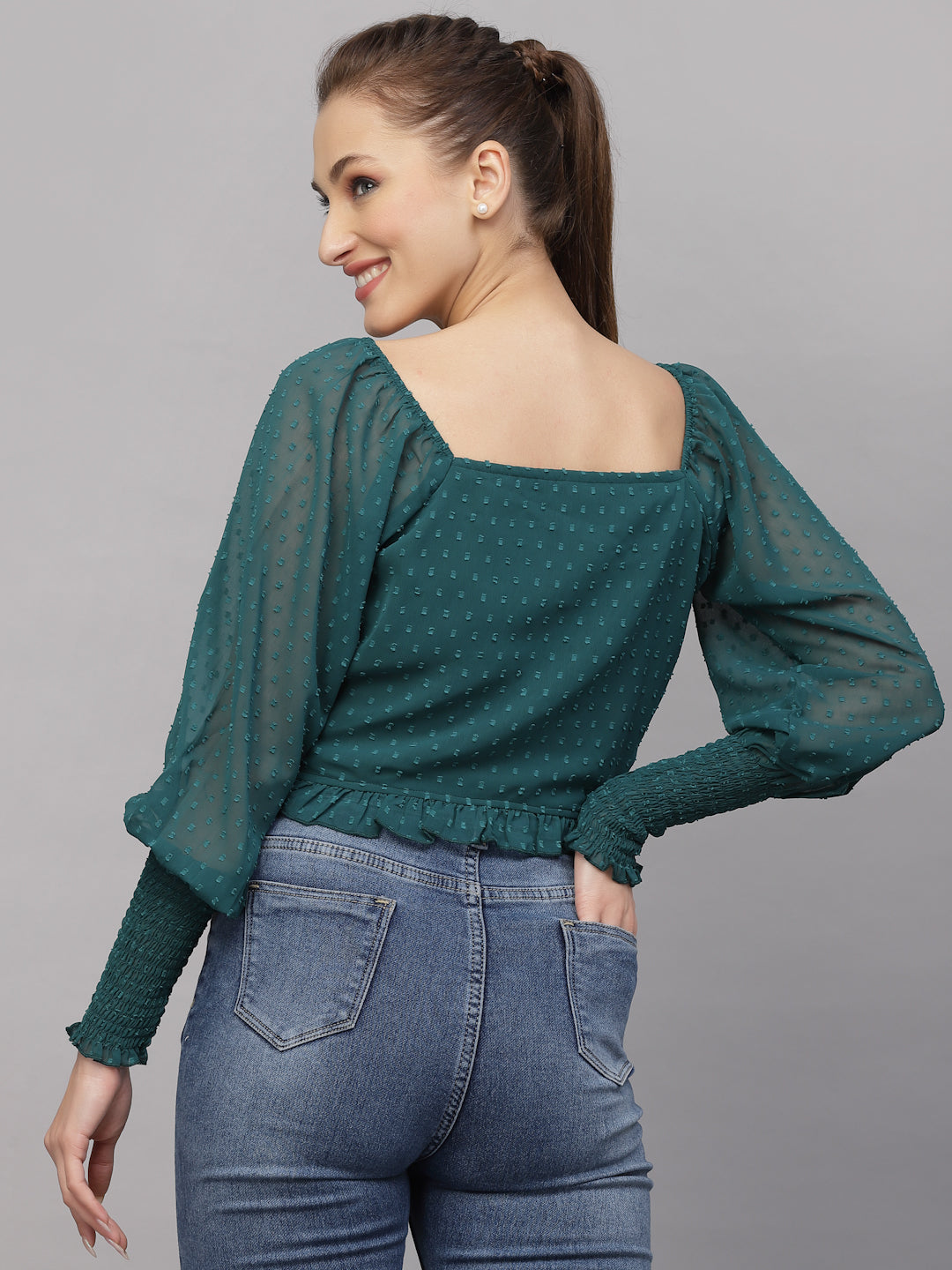 Woman wearing a green top with puffed sleeves and blue jeans on a gray background