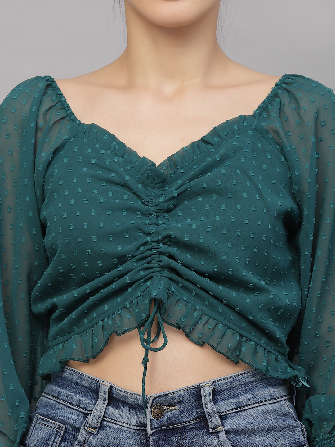 Green polka dot top with ruched design and blue jeans on a gray background