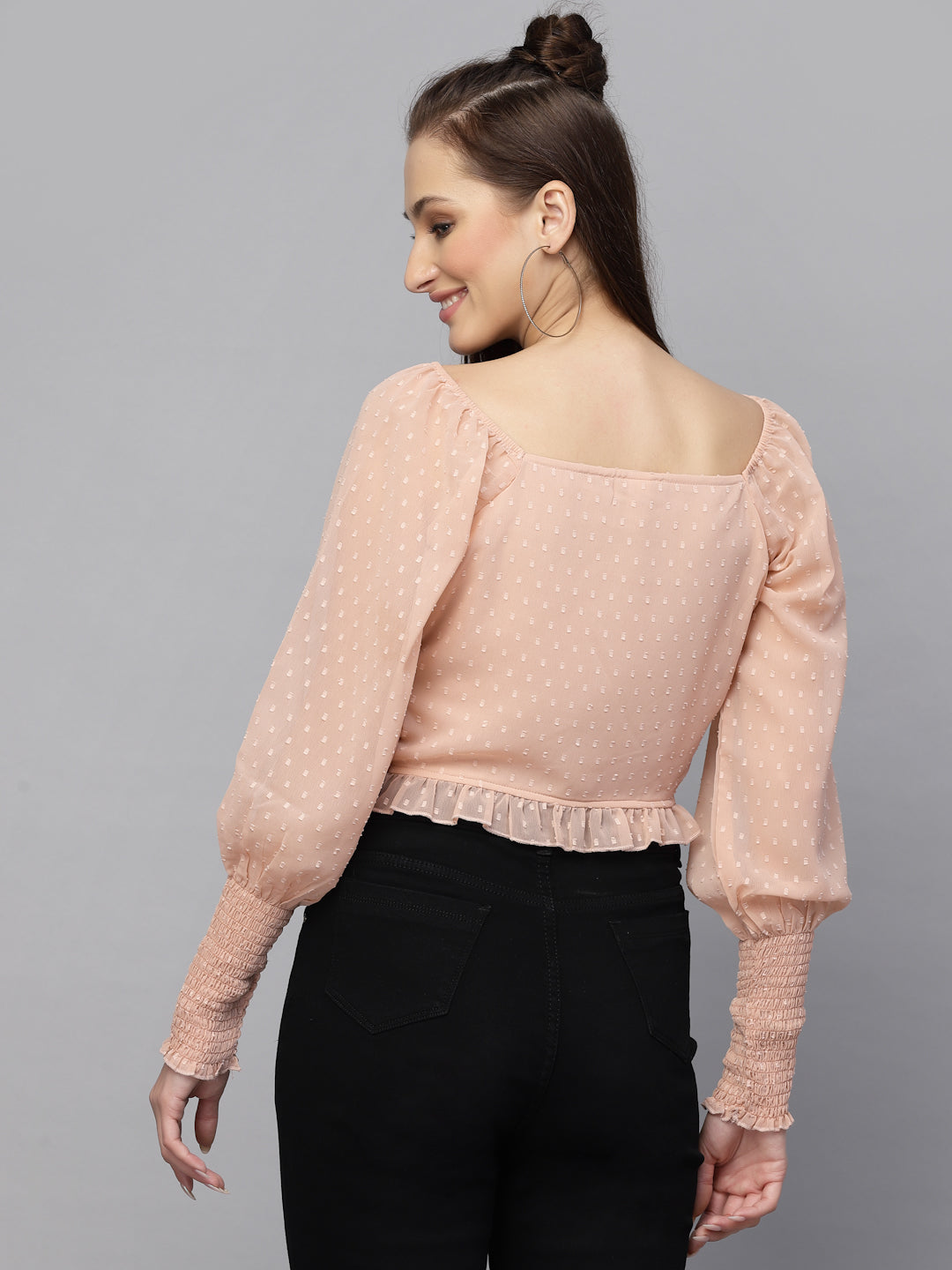 Woman wearing a peach top with long sleeves and black pants on a gray background