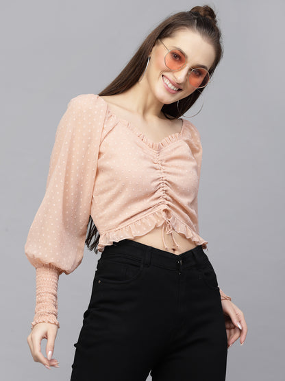 Woman wearing a peach top with ruffled details and black pants on a gray background