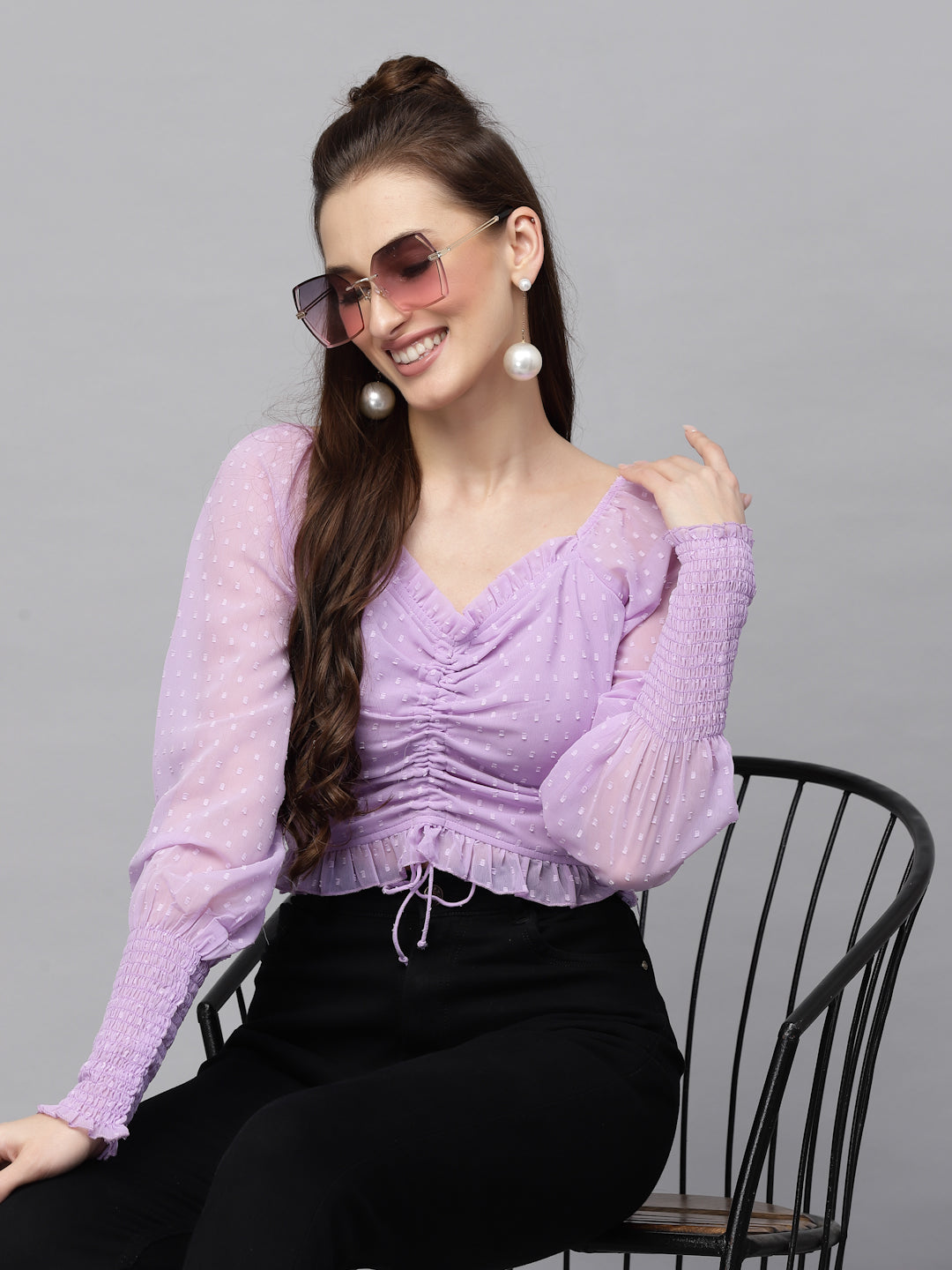 Woman wearing a purple top and sunglasses sitting on a chair against a gray background