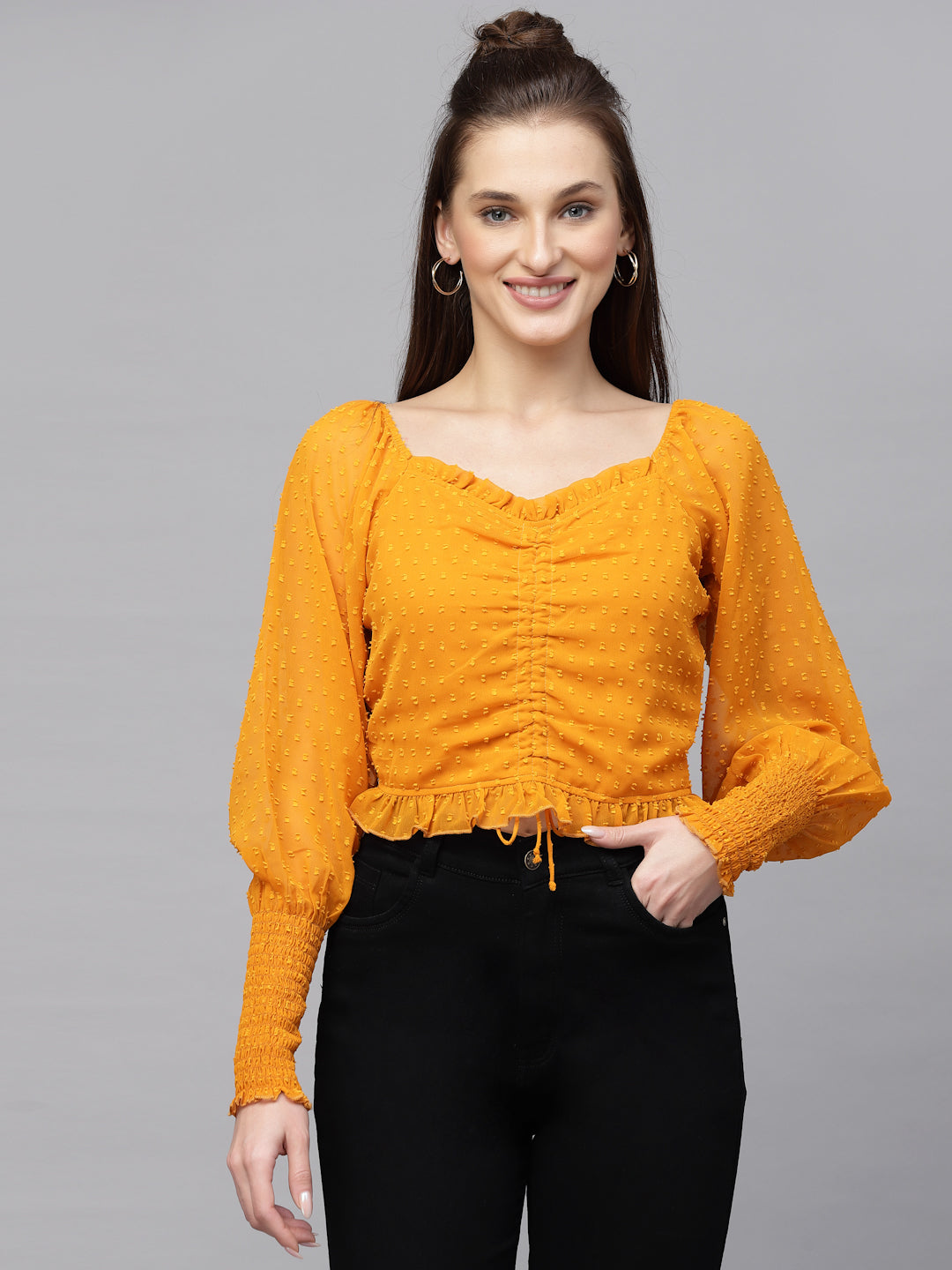 Woman wearing a mustard yellow top with long sleeves on a gray background