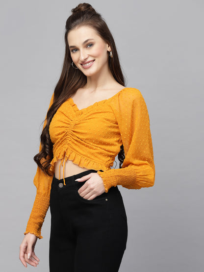 Woman wearing a mustard yellow top and black pants on a gray background