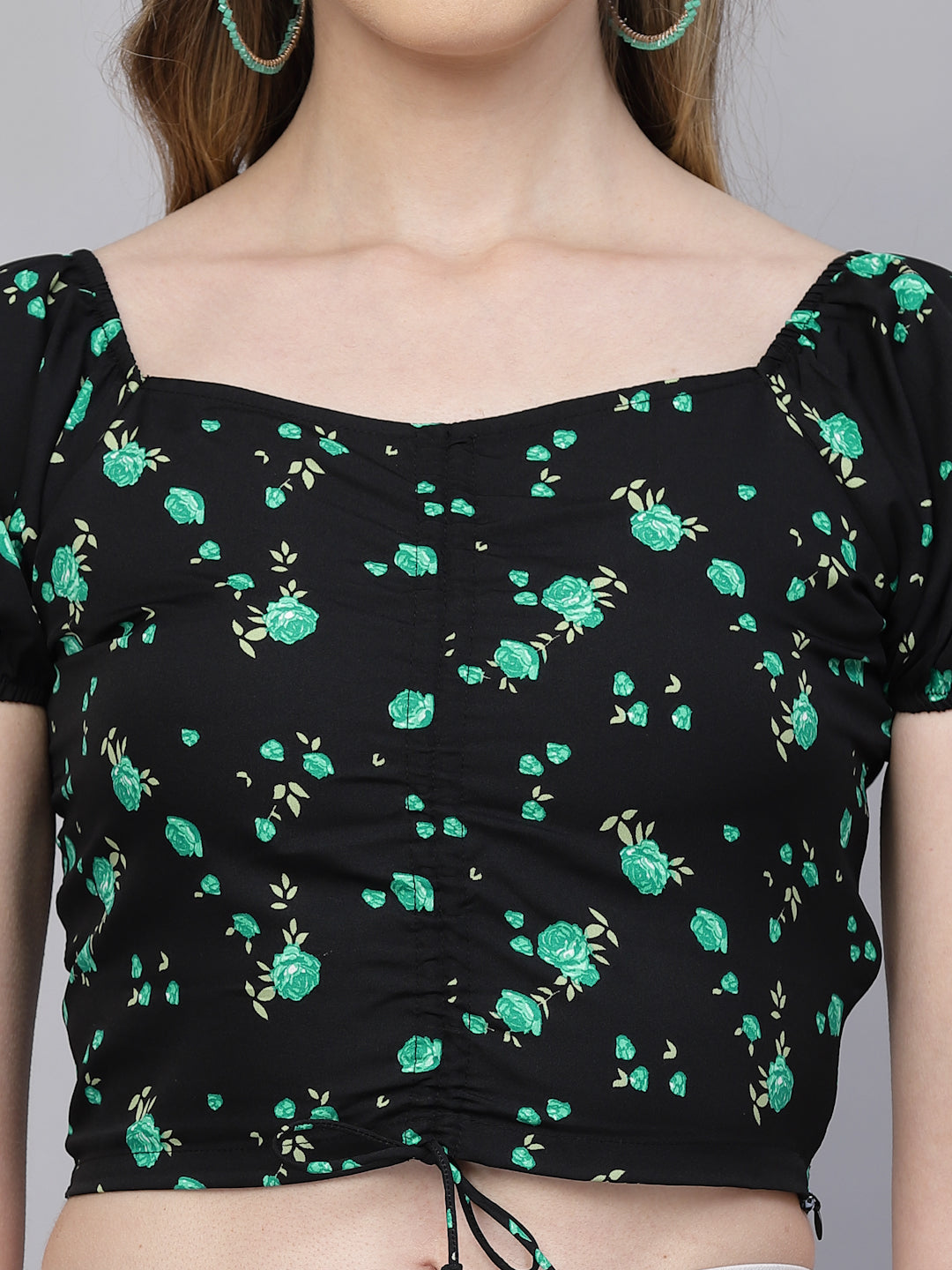 Black top with green floral pattern worn by a person on a gray background