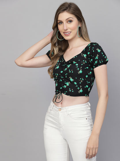 Woman wearing a black floral top and white pants on a gray background