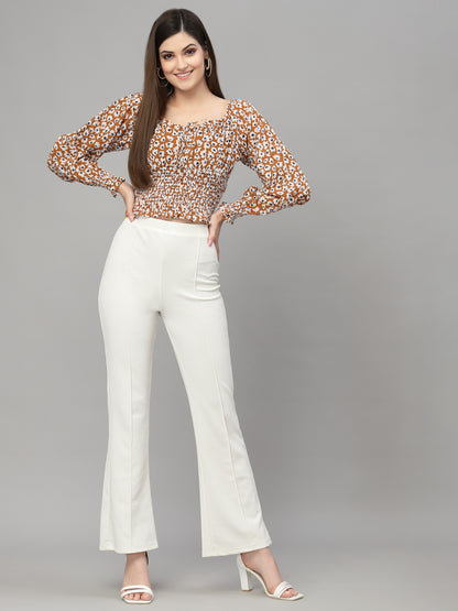 Woman wearing a brown floral top and white pants on a gray background