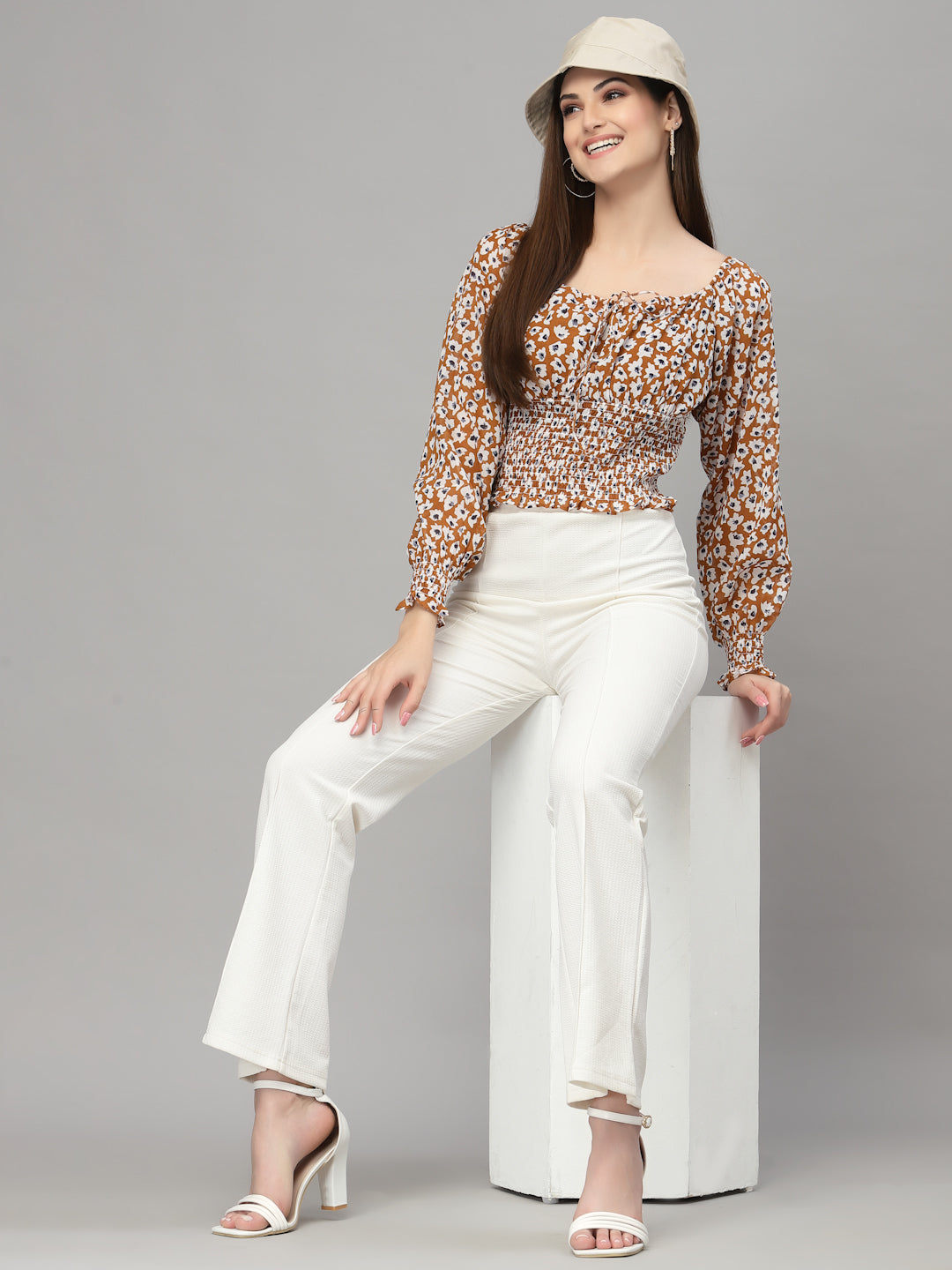 Woman wearing a brown floral top and white pants on a gray background