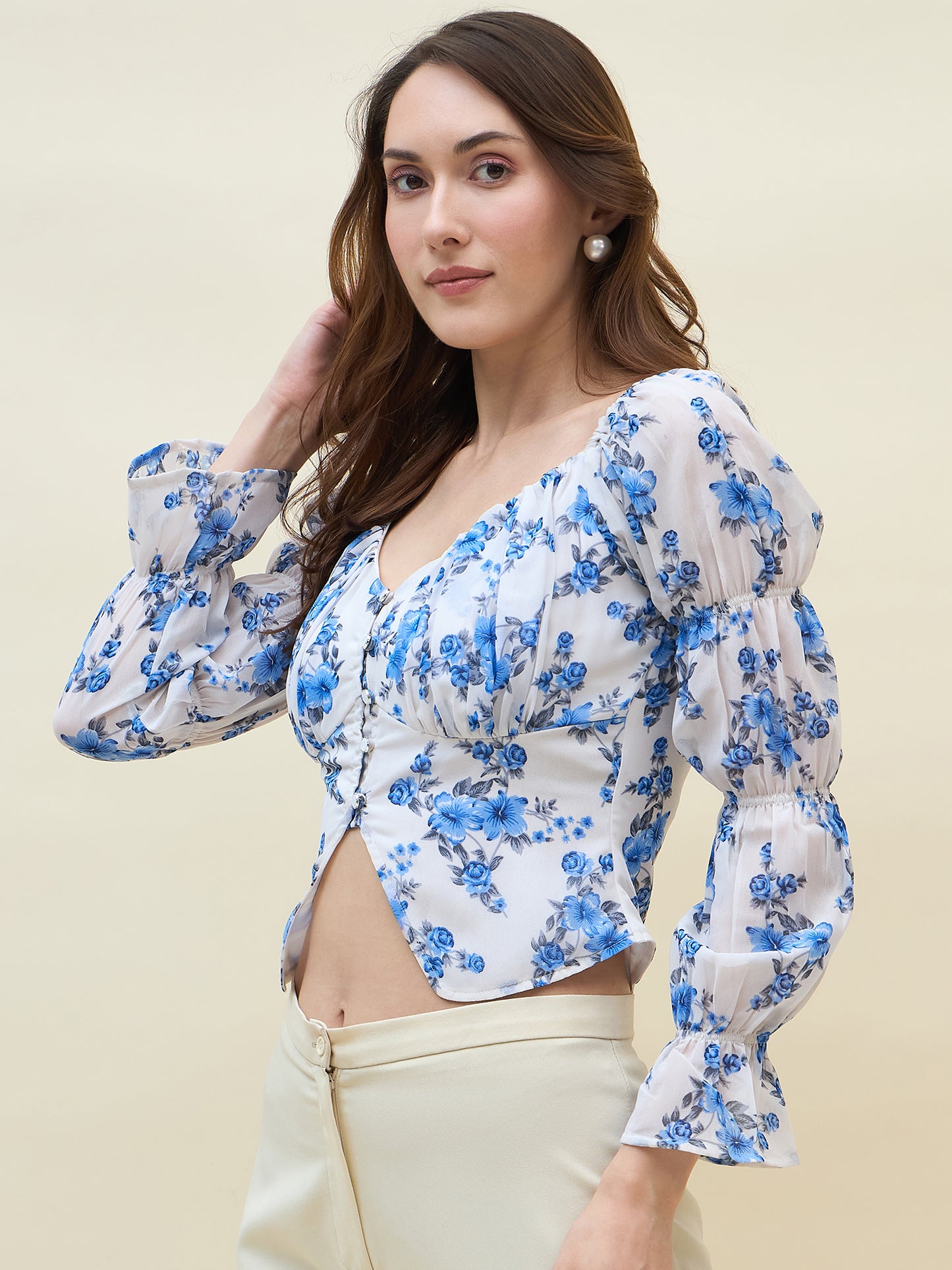 Woman wearing a white & blue floral top with puffed sleeves against a beige background