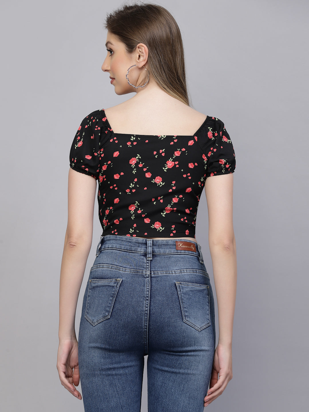Woman wearing a black & pink floral top and blue jeans on a gray background