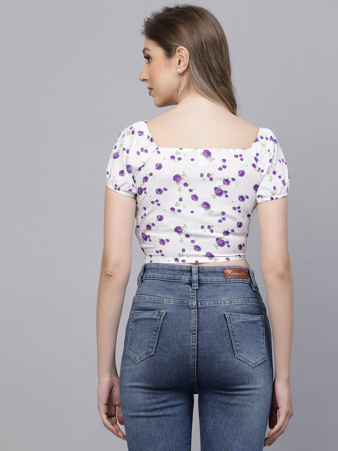 Woman wearing a white floral top and blue jeans on a gray background