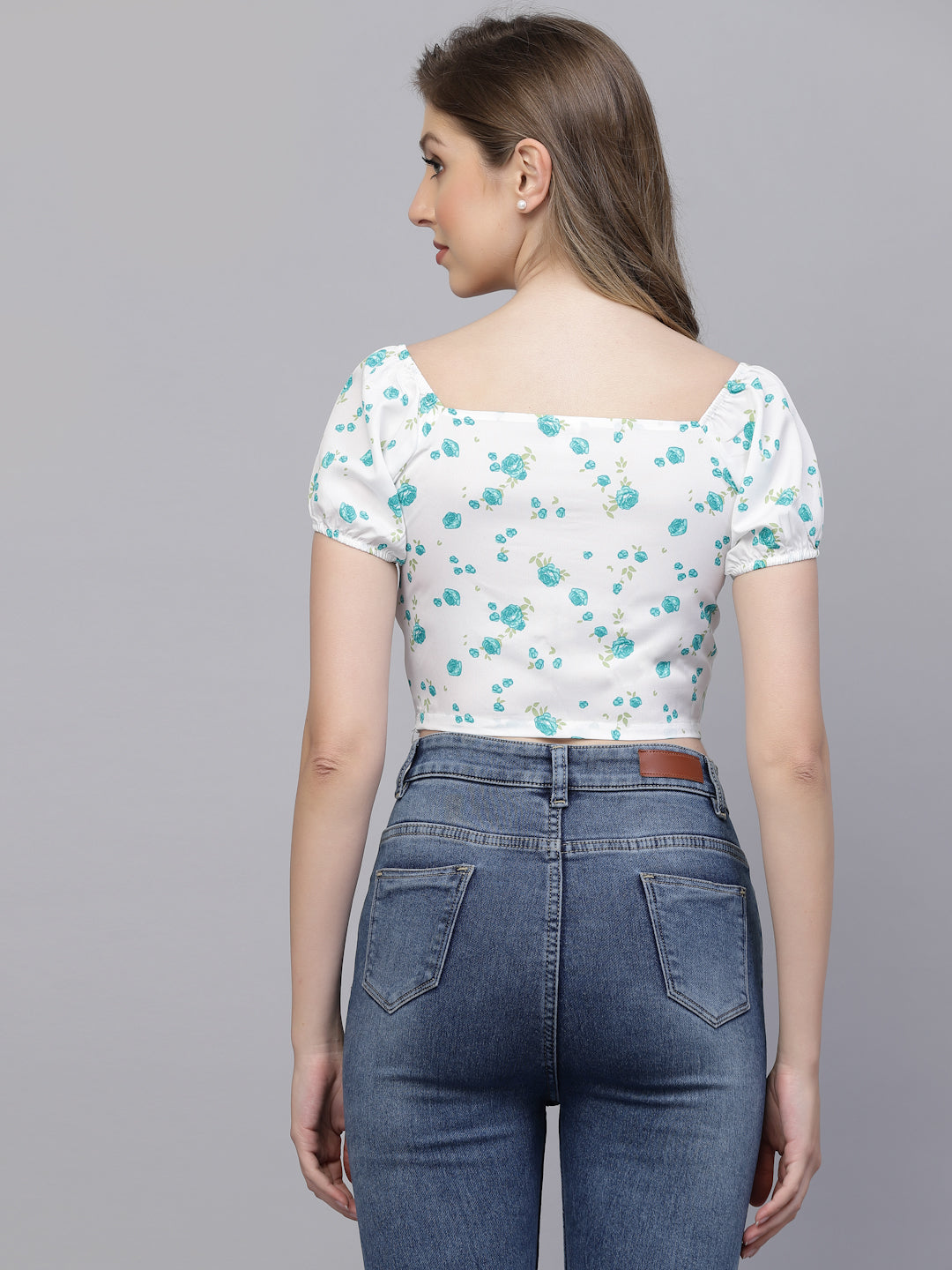 Woman wearing a white floral top and blue jeans on a gray background