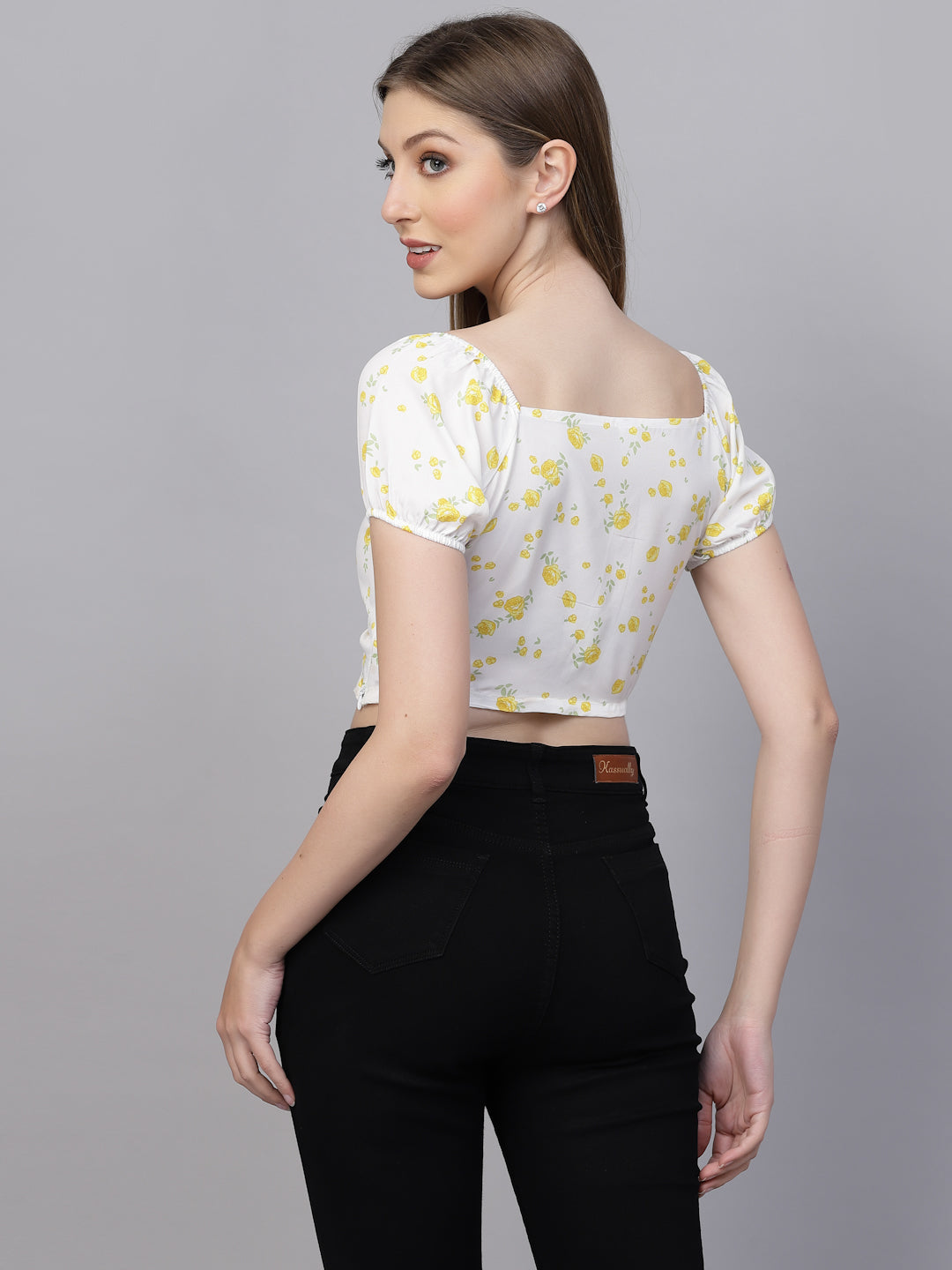 Woman wearing a white top with yellow floral patterns and black pants on a gray background
