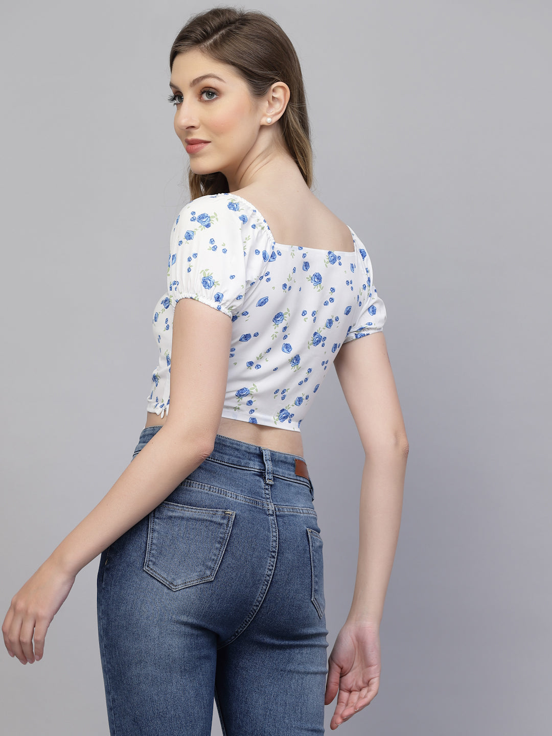 Woman wearing a white & blue floral top and blue jeans on a gray background